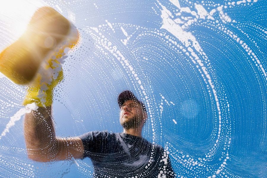 A man with a yellow sponge cleans a window, exemplifying the services offered by a window cleaning company.